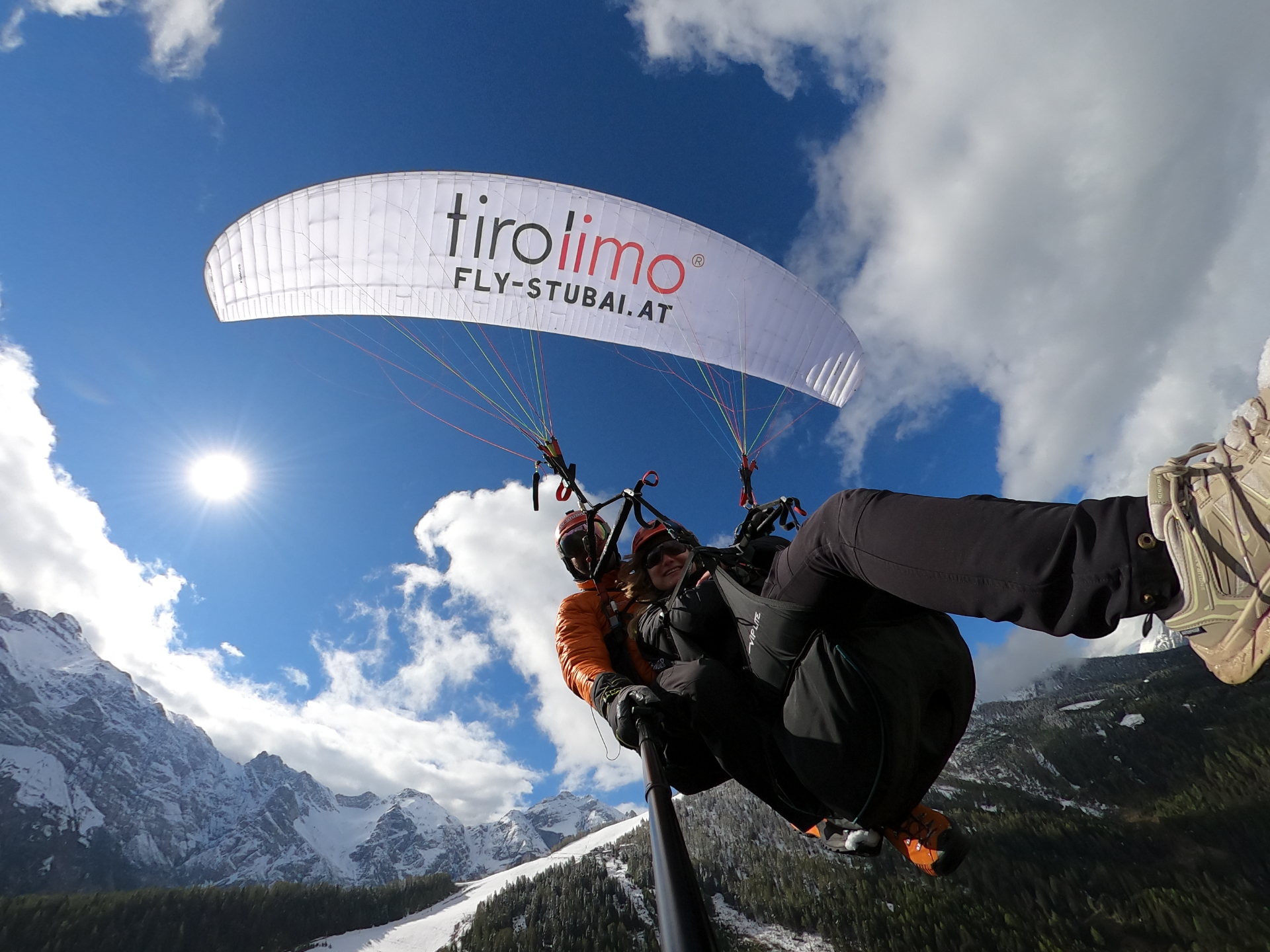 Lachender Tandemgast beim Paragliding über verschneitem Tal in Tirol