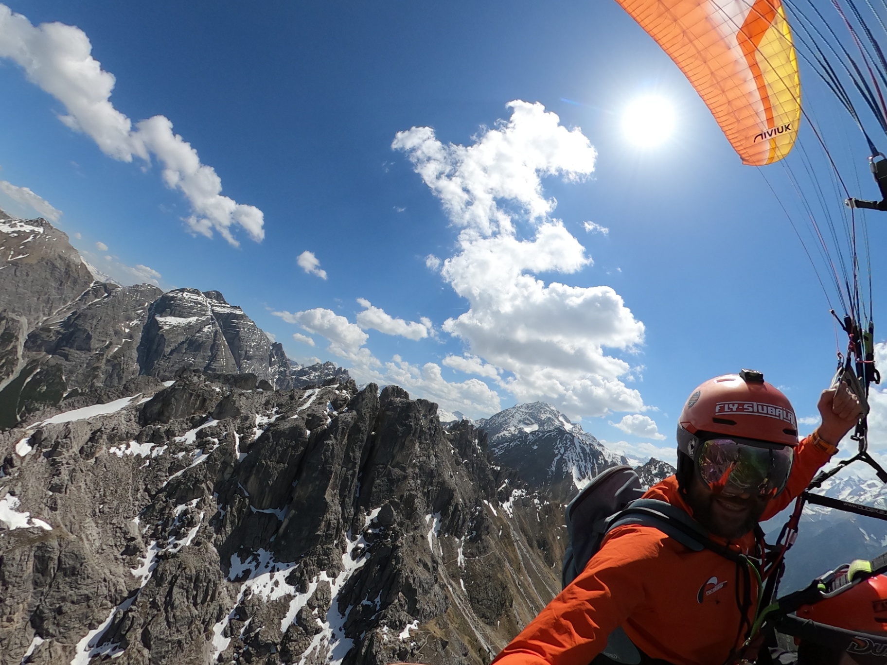 Pilot lächelt beim Tandem-Paragliding entlang schroffer Felsgrate in den Stubaier Alpen